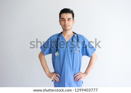 Content handsome young male physician posing at camera. Handsome guy standing and wearing blue medical uniform. Medicine concept. Isolated front view on white background.