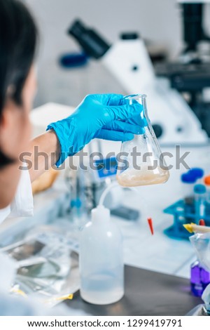 Hands in gloves of female scientist in laboratory shake glass flasks with dissolved samples of the soil. Agrochemical examination of soil.