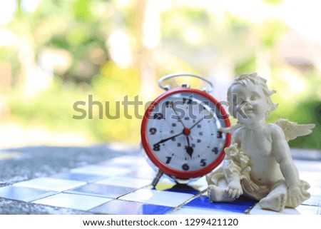 Close-up picture of doll cupids on marble floor alarm clock as background selective focus and shallow depth of field