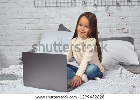 Cute little girl girl feeling amusing while watching cartoons on a laptop sitting on bed