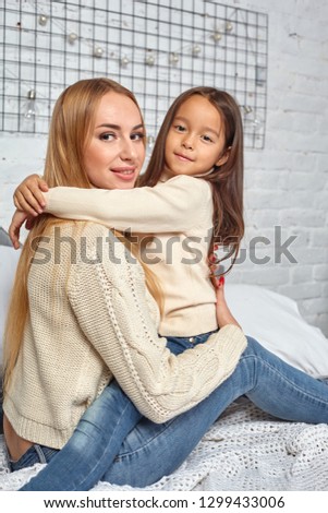 Beautiful young woman and her charming little daughter are hugging.