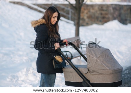 Young mother walking with her baby in pram. Beautiful stoller. Winter photosession
