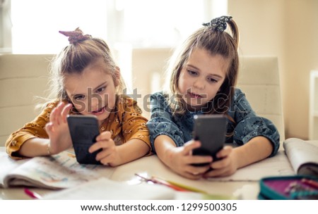 They each have their own tech toy. Two little school girls using smart phone.