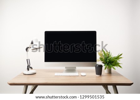 workplace with coffee to go, lamp, green plant and desktop computer with copy space isolated on white
