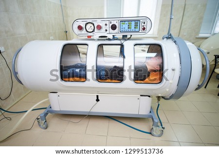 the guy in the black T-shirt lies in the hyperbaric chamber, oxygen therapy, medical room Royalty-Free Stock Photo #1299513736