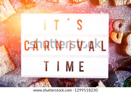Carnival concept, a lightbox with message " it's carnival time" illuminate circled by cookies and sweeties typical of carnival, like italian sfrappole or Chiacchiere, carnival fried pastry,flatlay