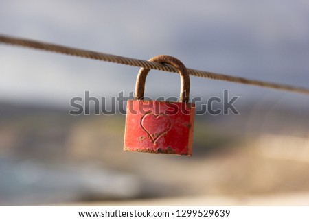 Red love padlock attached to steel wire. Rusty lock with heart shape carved hanging on railing outdoors. Valentines day, unity, memory concepts