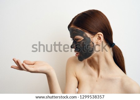 woman in a clay cosmetic mask holds and looks at the place free on a light background