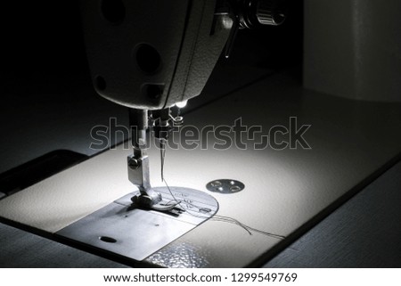 White industrial sewing machine with black background closeup.