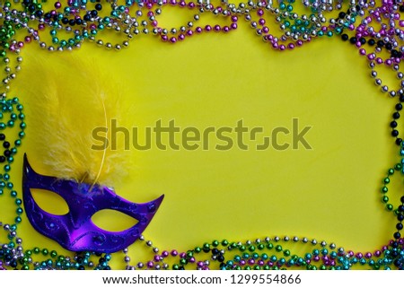 A yellow Mardi Gras background framed by colored bead necklaces with a Venetian mask in the corner.