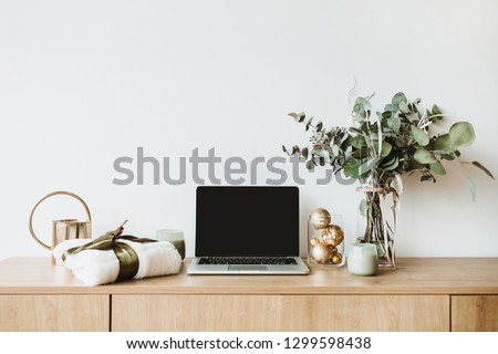 Blogger, freelance home office desk workspace. Laptop with mock up screen on wooden desktop decorated with eucalyptus bouquet, gift box, candles on white background. Blog, website hero header.