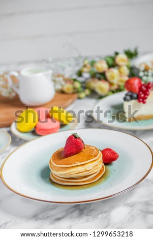 pancakes with tea, cheesecake and biscuits on a marble table with flowers