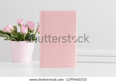 Pink book mockup with books and pink roses in a pot on a white table. Royalty-Free Stock Photo #1299660310