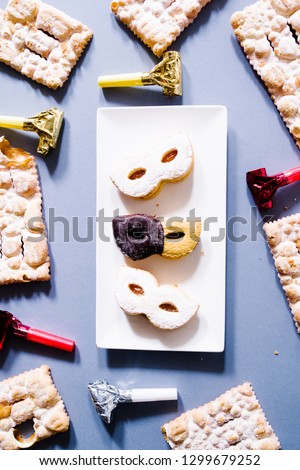 Carnival masks of short pastry with different decoration on a plate with whostlers and italian sfrappole  around on a gray  background