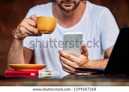 Man with smartphone, coffee / tea and laptop on a home porch.