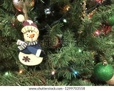 A jolly wooden snowman ornament hangs among the lights on a Christmas tree.