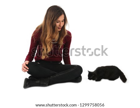 Young blonde woman playing with a black cat against a white background