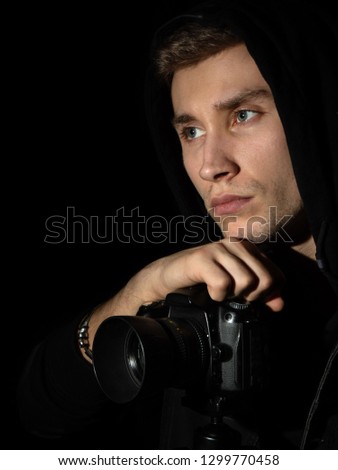 Man photographer with a DSLR camera on a tripod in a black hood in black background isolated