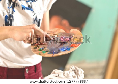Palette with colors in the hand of the girl. cleans off unnecessary paint. The concept of fine arts