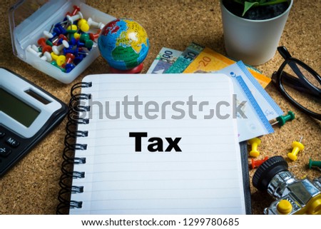 TAX inscription written on book with globe,eyeglasses, calculator, camera, pencil and vase on wooden background with selective focus and crop fragment. Business and education concept