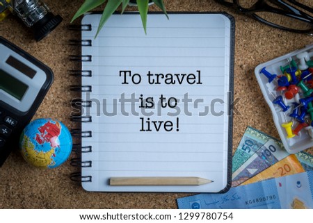 TO TRAVEL IS TO LIVE inscription written on book with globe,eyeglasses, calculator, camera, pencil and vase on wooden background with selective focus and crop fragment. Business and education concept