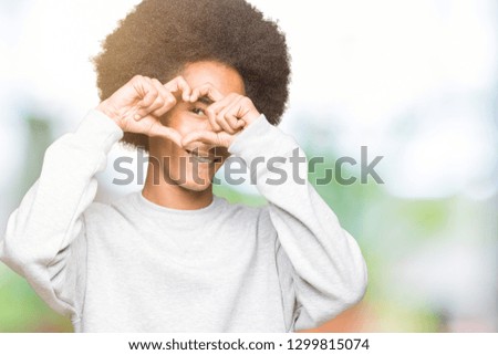 Young african american man with afro hair wearing sporty sweatshirt Doing heart shape with hand and fingers smiling looking through sign