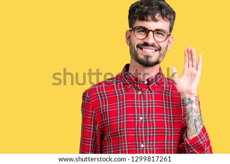Young handsome man wearing glasses over isolated background Waiving saying hello happy and smiling, friendly welcome gesture