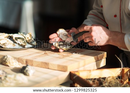 Opening the hollow and flat oysters. Chef opens oysters in the restaurant Royalty-Free Stock Photo #1299825325