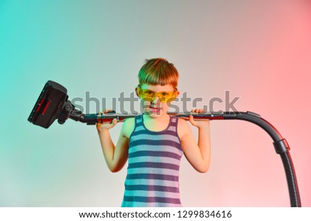 Cute baby raises the hose of the vacuum cleaner, photo in the studio.