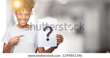 Young african american woman holding paper with question mark over isolated background very happy pointing with hand and finger