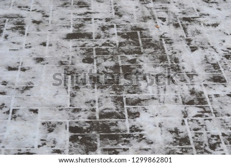 Closeup photograph of melting snow on a pavement made of gray concrete tiles.