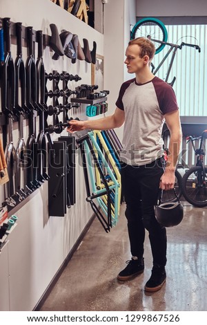 Vertical photo of a young man holding a protective helmet and choosing parts for his BMX in a bicycle shop
