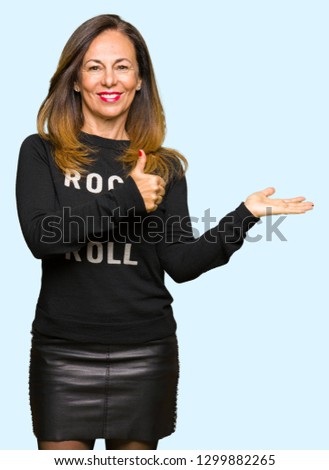 Beautiful middle age woman wearing rock and roll sweater Showing palm hand and doing ok gesture with thumbs up, smiling happy and cheerful