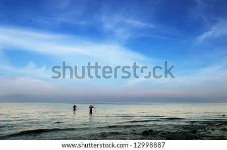 Early morning picture of two fishermen hunting for octopuses in the shallow waters of the Messinian bay, southern Greece