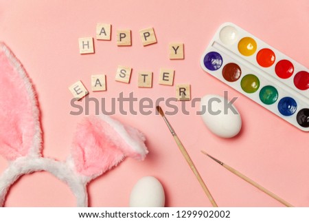 Happy Easter concept. Preparation for holiday. Inscription HAPPY EASTER letters eggs colorful paints and bunny ears isolated on trendy pink background. Simple minimalism flat lay top view copy space