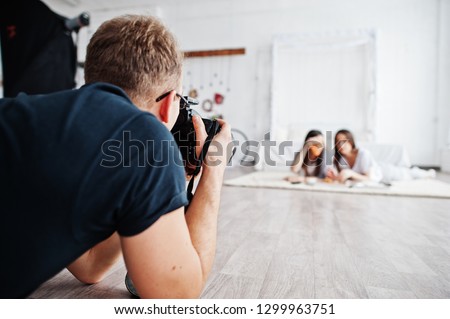 Man photographer shooting on studio twins girls who are eating pizza. Professional photographer on work.