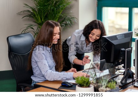 Two attractive female designers in blue shirts working together with new project on pc in the modern office. Team work concept.