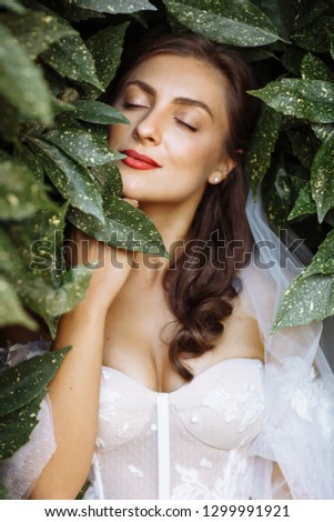 Close-up portrait of a very beautiful bride with wedding makeup, which is posing with eyes closed against the background of green leaves