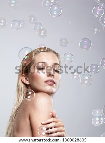 Beautiful young blonde woman with soap bubbles on grey background. Female with eyes closed.