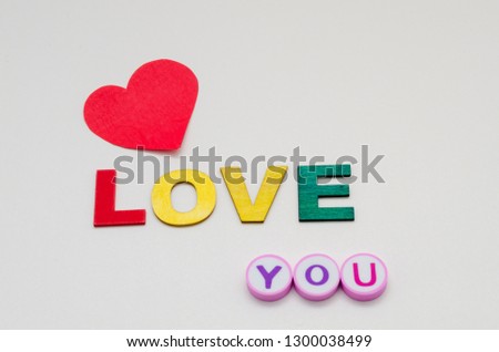 Love you phrase made from colorful letters made of wood and erasers and a paper red heart against white background