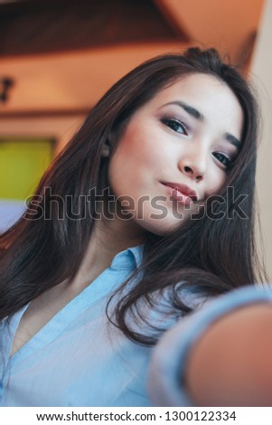 Beautiful charming brunette smiling asian girl taking selfie on frontal camera at cafe 