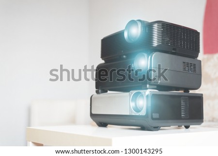 Many stacked projectors on a table on a sofa background.