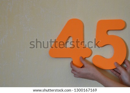 45 - hands holding orange number four and five or forty five on mild yellow wall background with copy space for text. 45th anniversary or birthday design.

