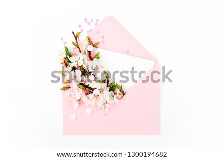 Pink envelope with empty card and a spring flower arrangement. Flat lay, top view.