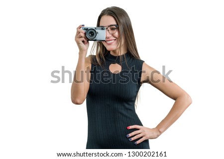 Young smiling beautiful woman in black dress glasses holding photo camera in her hands, taking photo, on white isolated background.