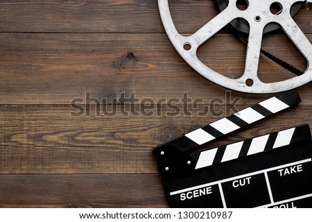 Filmings concept. Clapperboard and film stock on dark wooden background top view copy space