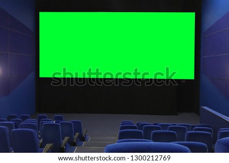 View of the empty cinema hall and a large green screen from the top rows. Cinema with rows of blue chairs