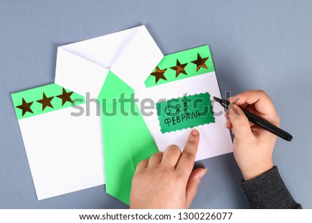 Diy white shirt paper with green tie, epaulets. Text in Russian - from February 23. Handmade. Step by step. process kid crafts. Top view. Greeting card on day defender fatherland.