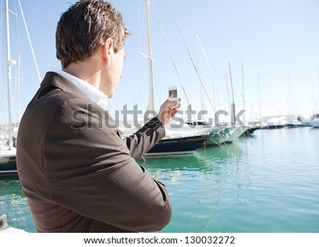 Close up of a businessman hand holding a "smart phone" up and taking pictures of a luxury yachts marine during a sunny day.