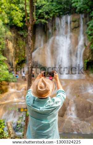 Green shirt man is taking a photo of waterfall by his mobile phone